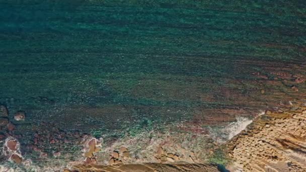 クリスタル海水洗浄粗い石造りの海岸トップビュー 落ち着いたターコイズの波がスーパースローモーションで空の岩の海岸線に飛び散る素晴らしい海岸 日光の下で熟した明確な海洋表面 — ストック動画