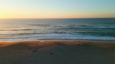 Muhteşem altın gün batımı gökyüzü güzel okyanus üzerinde yaz zamanı. Hava aracı gün batımından sonra inanılmaz deniz ufku. Sakin sörfler güzel kumlu kumsalda dönüyor köpükler saçan yavaş çekim. Deniz manzarası.