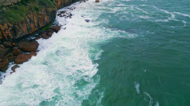 Kıyıdaki kayalıklarda ağır çekimde çarpan çarpıcı köpüklü deniz. Koyu deniz manzaralı dramatik okyanus dalgaları kıyı kayaları üzerinde kırılıyor. Manzaralı köpüklü su. Yıkayan sahil taşları..