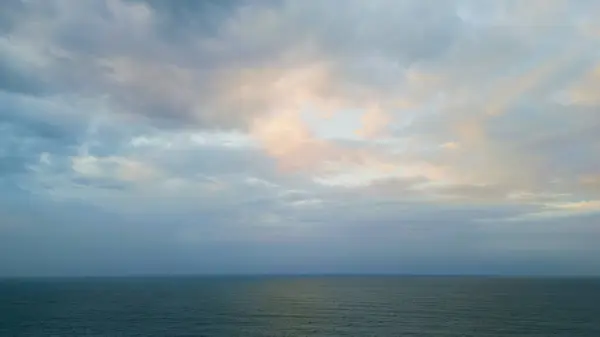 Dramatic sky over calm dark ocean at summer twilight. Sun rays breaking gray clouds over ripple sea water. Breathtaking gloomy seascape at evening dusk. Aerial panoramic view cloudy endless horizon.