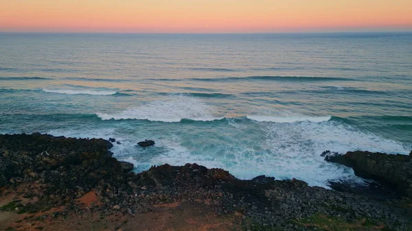 Pink sky ocean sunrise over picturesque foamy waves aerial view. Dramatic coastline landscape orange horizon over ripple sea water before dawn. Scenic calm surf rolling stone coast in slow motion.