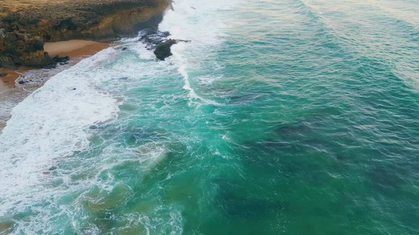 Drone view rough ocean waves crashing on coastal cliffs slow motion. Majestic sea surfs lapping on rocky beach. Aerial view fabulous tide breaking on seashore with white foam. Coastal nature scenery.
