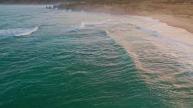 Şişkin, boş deniz kıyısında ağır çekim. Köpüklü turkuaz dalgaları olan sakin deniz kıyıları. Resimli derin okyanus sörfü manzarası. Yeşil su yüzeyi yaz havasında güneş ışığını yansıtır. 