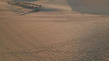 Gevşek kum, güneşli çöl havası. Islak kumun üzerinde uçan dron. Sinematik panorama parlak bej kumullar yeşil tepelerin siluetleri arka planda. Güneş ışığı plaj manzarasını yansıtıyor