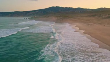 Köpüklü yeşil okyanus dalgalarıyla yıkanmış harika deniz manzarası. Gün batımından sonra güzel kumlu deniz kıyısının üzerinde gökyüzü. Manzaralı deniz sörfleri yavaş çekimde kıyı şeridinde dönüyor