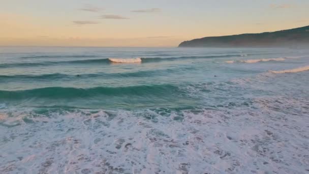 冲浪者在淡淡的天空的早晨在海浪中游泳 在日出下滚滚的海水在沙滩上飞溅 默默无闻的运动员在岸上享受周末 假日休闲概念 — 图库视频影像