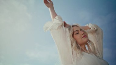 Yaz gökyüzündeki modelin portresi yumuşak güneş ışığını aydınlattı. Güzel, kaygısız bir kadın beyaz elbiseli, dışarıda kameraya el sallıyor. Rahat romantik kız doğanın tadını yakın planda çıkar. Kadın güzelliği..