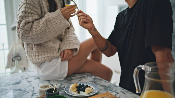 Муж кормит женщину ягодами на белом салоне крупным планом. Брюнетка пробует аппетитный завтрак из вилки с бокалом сока. Романтическая пара веселится на кухне. Любовные моменты
