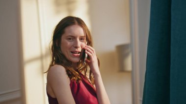 Konuşan neşeli kız aynaya yakından bakıyor. Mutlu kadın yansıması elbiseye hayran. Evde romantik bir randevuya hazırlanan neşeli, rahat, akıllı telefonlu bir bayan. Kendine güvenen çekici model..