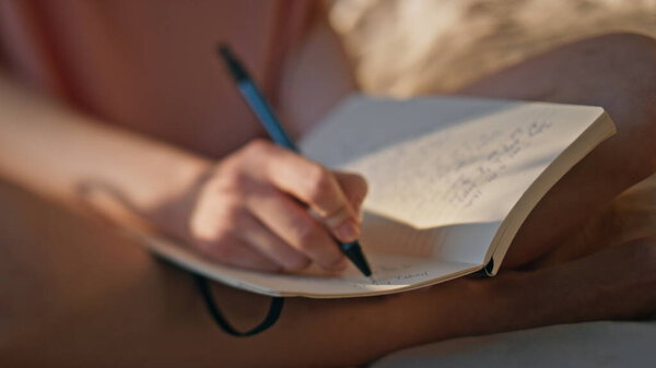 Hands writing personal journal in sunlight closeup. Calm girl rest morning bed noting creative ideas thoughts in diary. Unrecognized woman teenager holding pen making notes. Wish list schedule concept