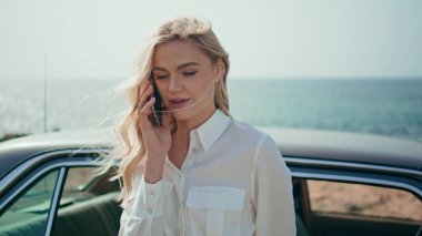 Kapanış konuşması yapan kız, güzel, güneşli okyanus kıyısında, retro otomobilin yanında duruyor. Çekici, mutlu bir kadının portresi. Yaz deniz kıyısında rahatlayan akıllı telefonlardan bahsediyor. Şirin sarışın, ara beni..