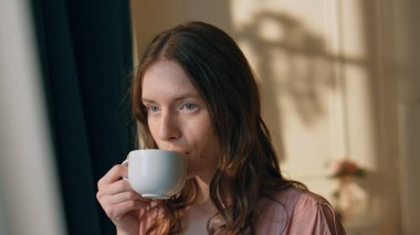 Hayalperest kız sabah güneşi altında kahve içiyor. Huzurlu, muhteşem bir manken evinde bir yudum alıyor. Güzel, gülümseyen bir kadın, soğuk havanın tadını çıkarıyor. Mükemmel hafta sonu rahatlama konsepti