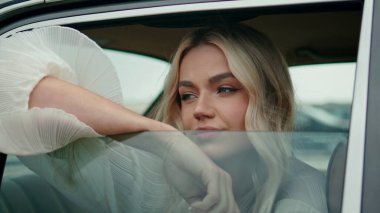 Model otomobil vitrininde poz veriyor, yakından bakıyor. Arka koltukta oturan çekici, rahat kadın portresi. Güzel sarışın kız açık araca yaslanıyor yaz rüzgarının tadını çıkarıyor..