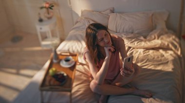Altın güneşli yatak odasından sabah kadın videosu. Rahat bir otelde dinlenen sakin bir kız rahat bir evde cep telefonuyla konuşuyor. Gülümseyen, gevşemiş ergen videoları yatakta akıllı telefon kullanıyor. Hafta sonu rutin konsepti