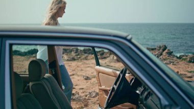 Kadın oto kuafördeki kolu çekerek kaputu açıyor. Ciddi kız sürücü güzel, güneşli deniz kıyısında duran arabanın motor sorununu kontrol edecek. Akıllı sarışın sürücü endişeli motor sorunu.