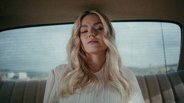 Arka koltukta oturan baştan çıkarıcı bayan klasik arabayı kapat. Güzel, kendine güvenen bir kadın rahat bir eski araba arka koltuğunda beyaz elbiseyle poz veriyor. Güzel sarışın model, gülümseyen bir kamera..