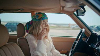Renkli bandanalı rahat bir kız otomobilde oturuyor. Yaklaş. Ön koltukta beyaz elbiseli, kaygısız genç sarışın poz veriyor. Çekici sakin kadın gülümseyerek kameraya bakıyor yolculuğun tadını çıkarıyor..
