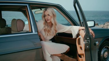 Şehvetli bir kadın deniz kıyısında güzel bir yaz haftasonunda ön koltukta oturuyor. Retro arabada poz veren çekici sarışın okyanus manzarasının tadını çıkarıyor. Tatlı genç bayan gezgin yol gezisinde dinleniyor..