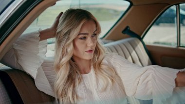 Arka koltukta oturan şık beyaz elbiseli bir kadın. Retro otomobilde rahatlayan güzel zengin bir kızın portresi. Çekici cazibe modeli otomobil salonunda poz veriyor. Seyahat kavramı.