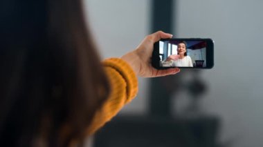 Akıllı telefondan video konferansı yapan mesafeli kadınlar. Kapanış kızı elleri cep telefonu ekranını tutuyor. Bilinmeyen bir bayan, hafta sonu ev ile ilgili haberleri paylaşıyor. Çevrimiçi iletişim kuran gülen arkadaşlar