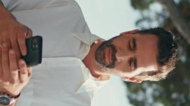 Rahat turist, akıllı telefonu dikey olarak kapalı tutarak şehir caddesinde yürüyor. Kaygısız yetişkin adam cep telefonu okuma mesajı kullanıyor. Yakışıklı gezgin, şehri geziyor, tatilin tadını çıkarıyor.