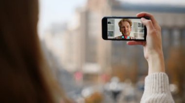 Uzaktaki ortakların videosu internetten arıyor. Kapalı el açık havada akıllı telefonu tutuyor. Gülümseyen adam sanal konferans uygulamasında konuşuyor. Tanımlanamayan kadın cep telefonuyla haberlerini paylaşan mutlu adamla sohbet ediyor.