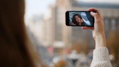 Videocu kız, akıllı telefon ekranına öpücük yolluyor. Mutlu arkadaşlar web konferansını haber paylaşma olarak adlandırır. Cep telefonunu tutan tanınmamış eller. Neşeli kadın caddede sanal toplantı yapıyor..