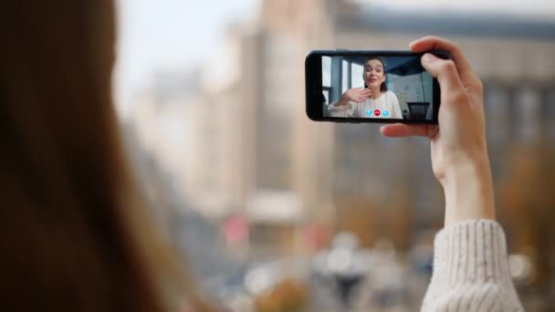 ストリートガールのビデオは 友人のクローズアップと呼ばれています 仮想会議アプリでスマートフォン画面を振る笑顔の女性 市内で携帯電話を持っている未知の女性の手 Joyful ガールフレンド チャット オンライン — ストック動画
