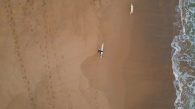 Bilinmeyen yürüyen sörfçü drone manzaralı tropikal plajlar. Güzel okyanus dalgaları altın kumsalda ağır çekimde yuvarlanıyor. Deniz kıyısına basan sörf tahtası taşıyan tanınmamış biri.