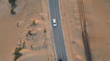 Üst manzaralı asfalt karayolu kum çölünü geçiyor. Yaz günü kırsal yolda çeşitli arabalar sürüyordu. Kum taşı çevresinden geçen kırsal yol kuru, alçak yeşillikle dolu. Trip konsepti