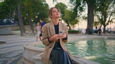 Kaygısız bayan, akşam çeşmede oturup akıllı telefonlardan konuşmaktan hoşlanır. Sosyal medyada şehir meydanında şık bir iş kadını mesajı. Güzel neşeli kız haberleri paylaşıyor.