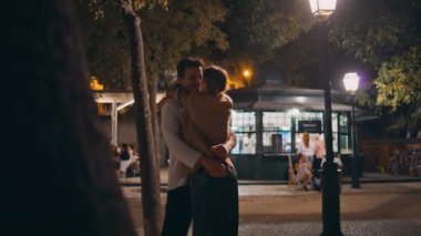 Sevimli aşıklar gece vakti buluşmayı kucaklıyor. Aydınlanmış cadde. Mutlu aile akşamları kucaklaşarak eğleniyor. Dışarıda öpüşen sevimli bir çift. Gece konseptinde sevecen romantik insanlar