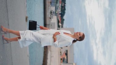 Bayan, deniz kenarında dikey bulutlu bir günde yürümeyi sever. Suyun yanındaki asfalt yolda şık elbiseler içinde gezen zarif bir iş kadını. Keyifli, rahat bir kadın gülümsüyor Koyun kıyısında kasvetli bir akşamda