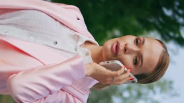 Rahat iş kadını sakin bir yerde cep telefonunu arıyor. Yeşil Park dikey meleği yaklaş. Çekici, zarif bir bayan akıllı telefondan konuşuyor. Yürüyüş sırasında dinleniyor. Cep telefonuyla başarılı bir yönetici danışmanlığı