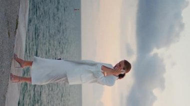 Başarılı iş kadını okyanus günbatımında dikey olarak gökyüzünden sesleniyor. Beyaz takım elbiseli zarif bir bayan deniz kenarında akıllı telefonlardan konuşuyor. Güzel bir akşam. Kendine güvenen bir kadın rıhtımda iş görüşmesi yapıyor..