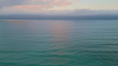 Dalgalanan okyanus yüzeyi güzel günbatımını yansıtıyor. Karanlık deniz suyunda yavaş çekim parlayan parlak altın ışınlar ile hava manzaralı deniz gündoğumu. Gün batımı bulutların arasından doğan güneş ışığı 