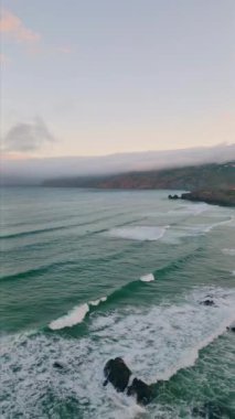 Harika deniz manzarası köpüklü yeşil okyanus dalgalarıyla yıkanmış. Güzel turkuaz fırtınalı su üzerinde havadan resimli pastel gökyüzü. Manzaralı deniz sörfleri yavaş çekimde kıyı şeridinde dönüyor