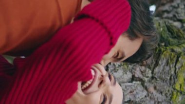 Gülen güzel bir çift, orman ağacının yanında dikey çekim yaparak tatillerini geçiriyorlar. Mutlu, gülümseyen bir çift doğa parkında keyif çatıyor. Neşeli iki insan hafta sonunun tadını çıkarır.