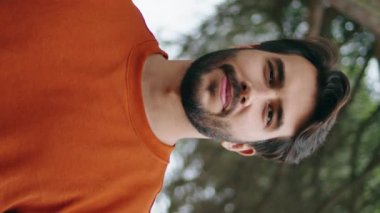 Yeşil Park 'ta kameraya gülümseyen yakışıklı sakallı adam. Sırt çantası taşıyan çekici bir gencin dikey portresi doğaya takılıyor. Ormandaki ağaçların önünde tek başına duran mutlu bir turist..