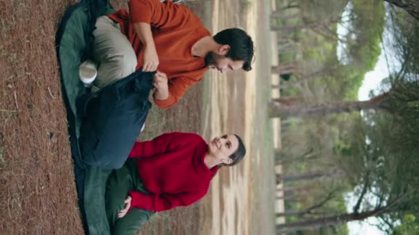 一对年轻无忧无虑的夫妇坐在毛毯秋天的森林上垂直向上 快乐轻松的游客准备野餐 从背包里取食 微笑的家人在公园享受浪漫的周末 — 图库视频影像