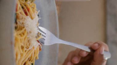 Kimliği belirsiz bir adam dikey olarak spagetti yiyor. Mumları olan zarif bir masa. Kadın elleri peynirle süsleme yapıyor. Çatal tutan adam romantik bir akşam yemeği yiyor.