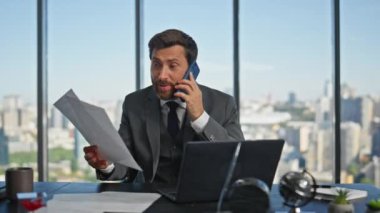 Sinirli girişimci panoramik ofiste cep telefonuyla iletişim kuruyor. Çılgın şirket patronu duygusal konuşma problemi yaşıyor. Sinirli işadamı evrak atıyor.