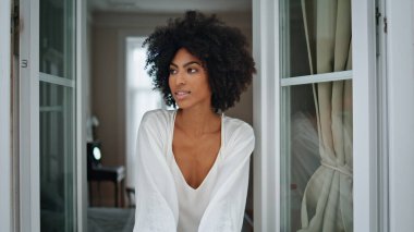 Haftasonu sabahları pencereye bakan rahat bir bayan. Koyu tenli, rüya gibi bir model kameraya bakıyor ve düz bir alanda dinleniyor. Portre esmer Afrikalı kadın ipek bornozlu günün tadını çıkarıyor. Ev hayatı konsepti