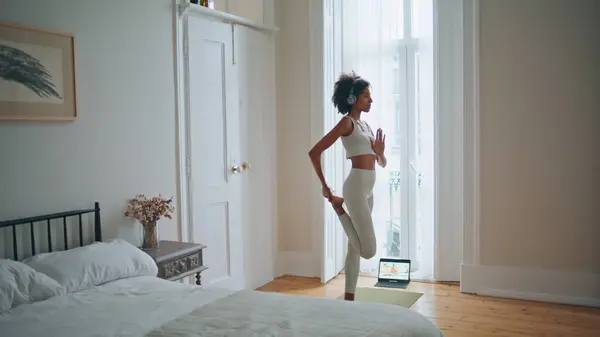 stock image Meditating model practicing yoga at bedroom. Dark skin grace lady exercising alone listening headphones music. Focused sportswoman performing asana at morning apartment. Fitness leisure time concept 