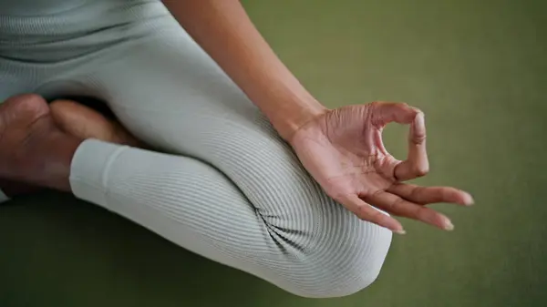 Yoga lady zen fingers connecting in lotus position close up. Unknown girl in leggings sitting crossed legs on sport mat. Sportswear woman hands meditating at home practicing asana. Calmness harmony