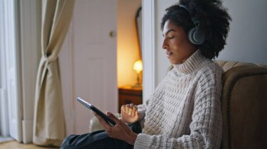 Serene denen kadın akşam apartmanına yakın çekim yapıyor. Sakin kulaklıklı kadın gözlerini kapattı ve alacakaranlıkta tablet müziğin tadını çıkarıyor. Kıvırcık saçlı kız hafta sonu evde dinleniyor. Afrika model tutucu bilgisayar