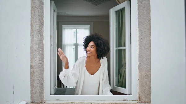Black hair girl waving window at morning house. Curly smiling woman looking at weather peeping outside. Happy african american model watching cityscape enjoying dreaming at home. Daily routine concept