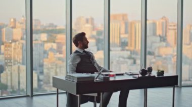 Memnuniyetli iş adamı ofis akşamında işi bitiriyor. Rahat yönetici ellerini başının arkasına koy ve şehir günbatımında proje sonuçlarının tadını çıkar. Başarılı bir avukat gelecekteki iş başarısını düşlüyor..