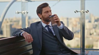 Başarılı bir adam cam terasta kahvenin tadını çıkarıyor. Sakin patron takım elbiseli yönetici sakin bir sabah istirahatgahında ofis balkonunda şehir manzarası seyrediyor. Yakışıklı orta yaşlı iş adamı. İçeceğini yudumluyor.