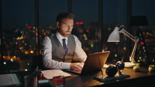 パノラマオフィスの夜景でラップトップを入力するデータを検索する遅いビジネスマン 集中した思慮深い労働者は夜にオンラインで働く残業時間を分析します ストレスを受けた金融専門家 — ストック動画